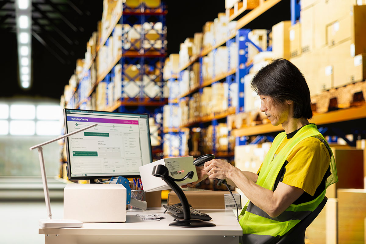asian depot worker scanning barcodes packages warehouse reviewing shipping labels